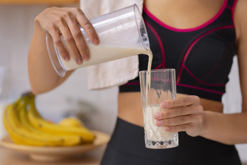 Kobieta w sportowym stroju nalewająca koktajl białkowy do szklanki – sposób na wygodne spożycie odżywki białkowej whey