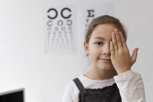 jak wyleczyć krótkowzroczność u dzieci – dziewczynka zasłaniająca oko dłonią do badania na wadę wzroku