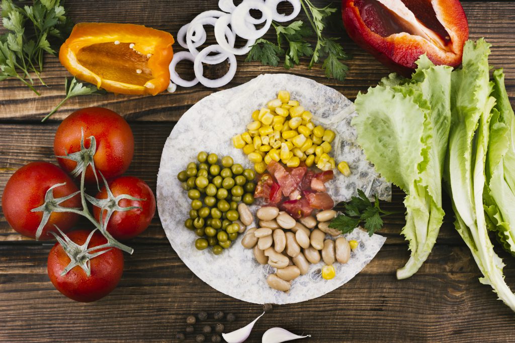 Kolorowe warzywa, fasola, kukurydza i sałata ułożone na tortilli – zdrowe składniki idealne na wysokobiałkową dietę wegetariańską.