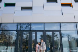 Młoda para stojąca przed eleganckim budynkiem z aluminiowo-szklanymi ramami – stylowe i trwałe okna Veka Katowice.