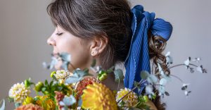 Kobieta trzymająca bukiet chryzantem z kokardą na włosach, w tradycyjnej fryzurze, z widoczną gumką z kokardą