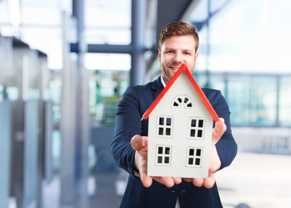 Mężczyzna trzyma domowy model domu w biurze, symbolizując inwestycję w dom maklerski