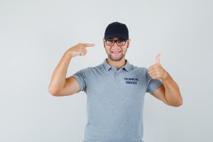 Młody technik w odzieży roboczej z logo, uśmiechnięty i pokazujący rękami detale stroju.