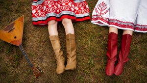 Widok na stopy dwóch osób w folkowych spódnicach i wysokich butach, obok leży tradycyjny instrument muzyczny