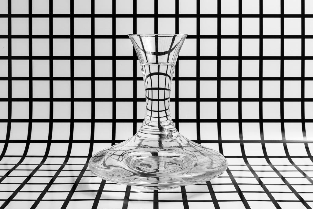 Szklane naczynie laboratoryjne na tle geometrycznej siatki, wykorzystywane w procesach kontroli jakości, powiązanych z sita laboratoryjne Brzesko.