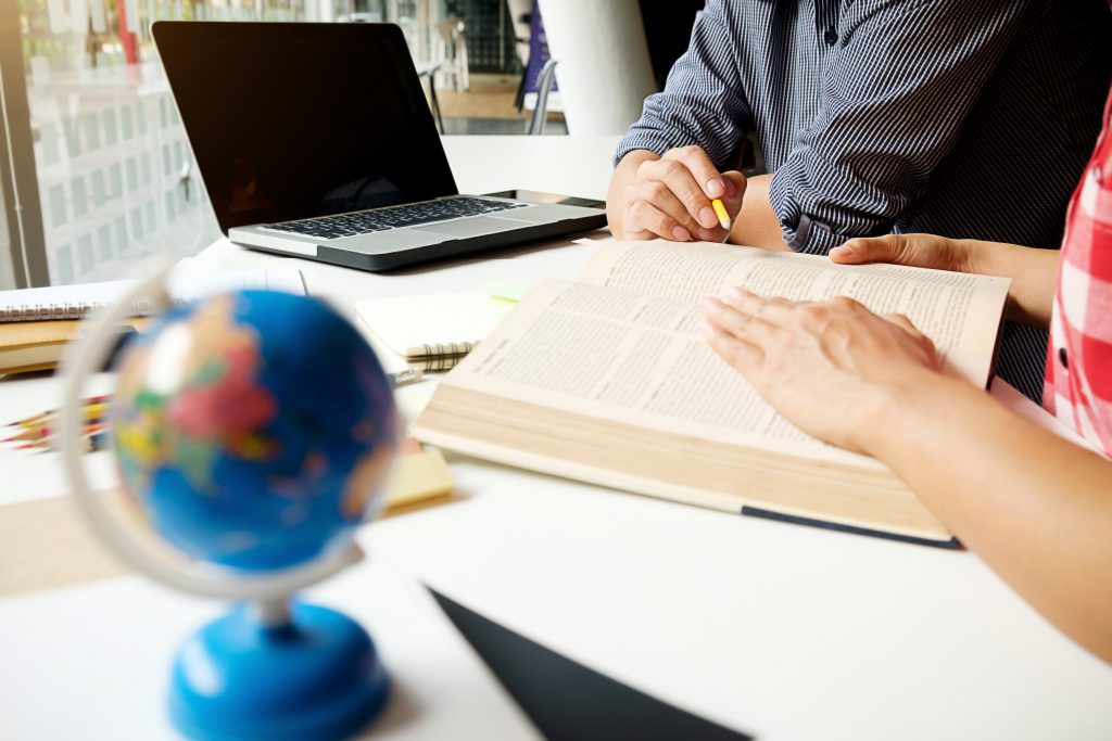 dwie osoby pracujące nad technicznym tłumaczeniem słowackim, siedząc przy biurku na którym jest laptop, globus i książki