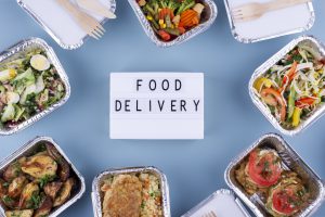Różnorodne posiłki w pudełkach ustawione wokół napisu food delivery – catering z dowozem