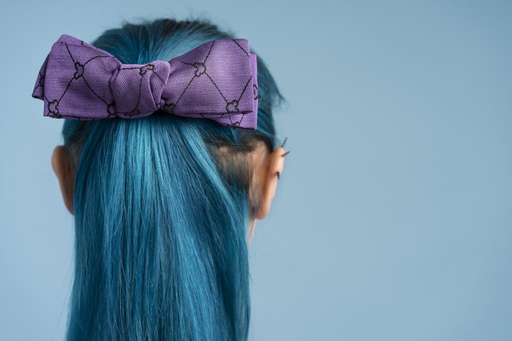 Kobieta z włosami związanymi gumką z kokardą w kolorze fioletowym, widok z tyłu