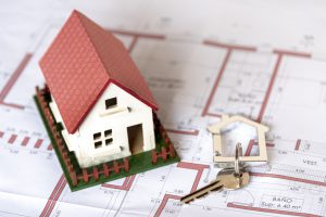 Dom inwestycyjny w makiecie z kluczami obok planu budynku, pokazujący koncepcję inwestycji w nieruchomości