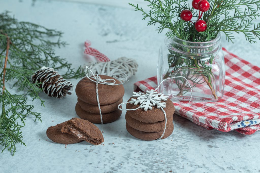 słodycze na Boże Narodzenie – czekoladowe ciasteczka z ozdobami świątecznymi na tle zielonych gałązek
