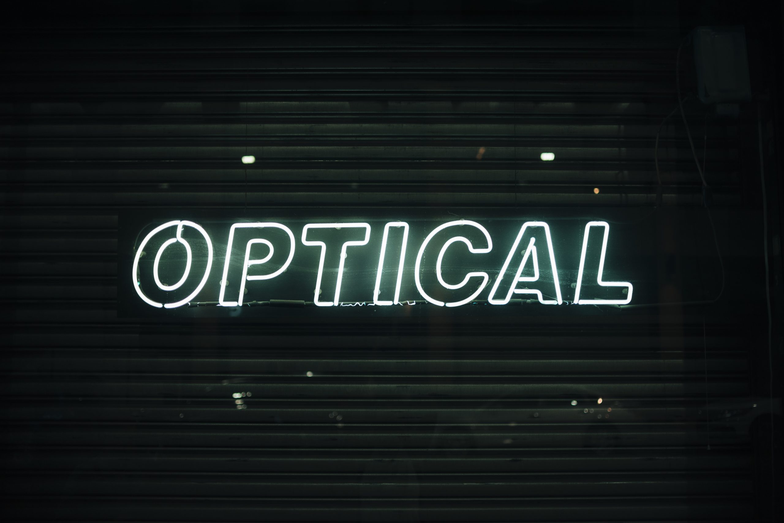 Podświetlane logo na ścianę w formie białego neonu z napisem OPTICAL