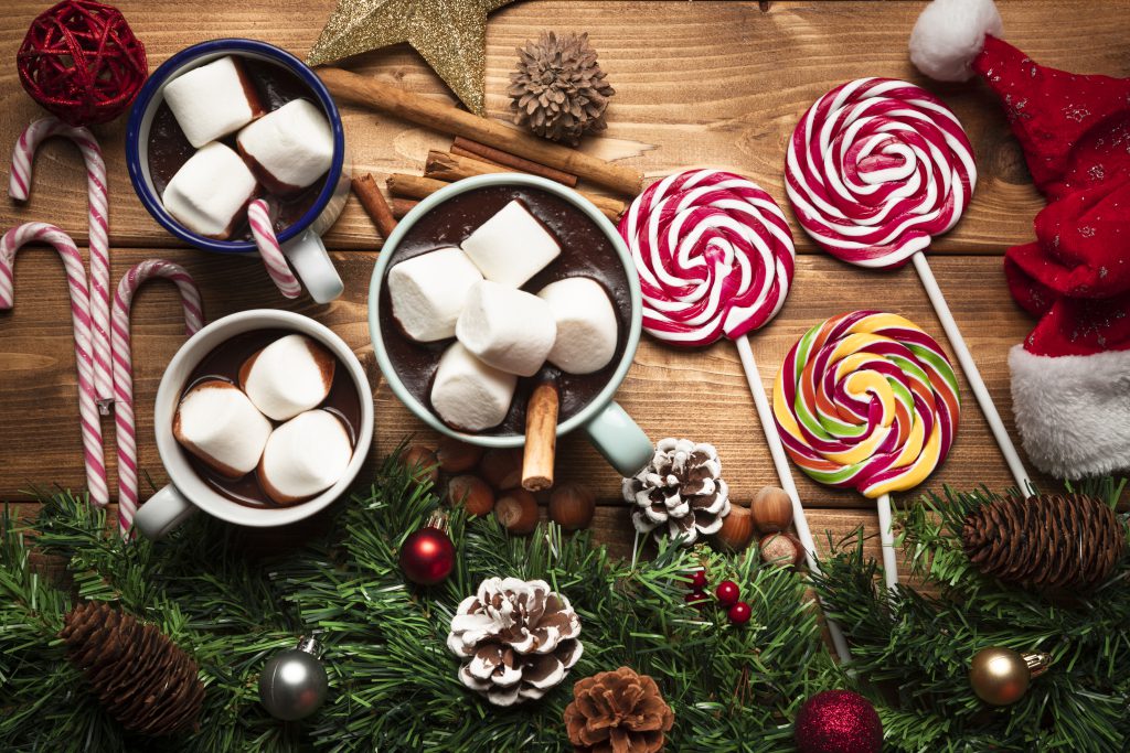 Słodycze na święta – kubki gorącej czekolady z piankami marshmallows, lizaki i laskowe cukierki na drewnianym stole