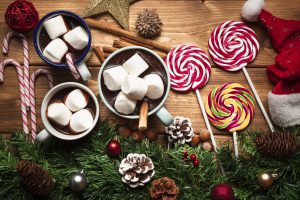 Słodycze na święta – kubki gorącej czekolady z piankami marshmallows, lizaki i laskowe cukierki na drewnianym stole