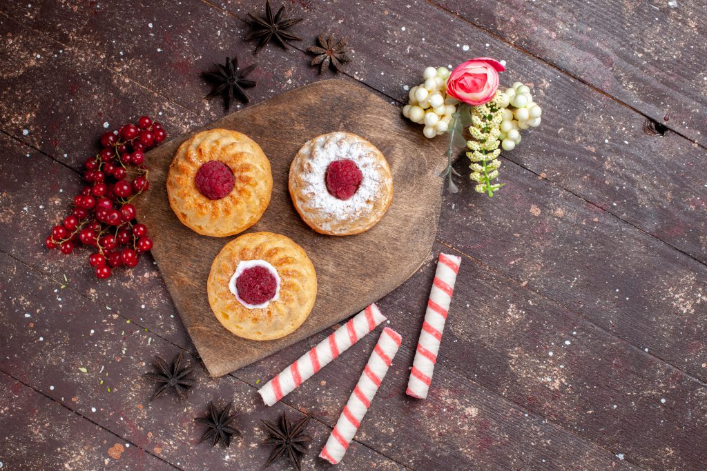 Słodycze na święta – małe ciasta z malinami, świeża żurawina i rurki waflowe na drewnianej desce